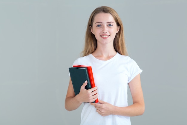 Estudiante joven con libros, libros de texto en las manos, aislado en gris