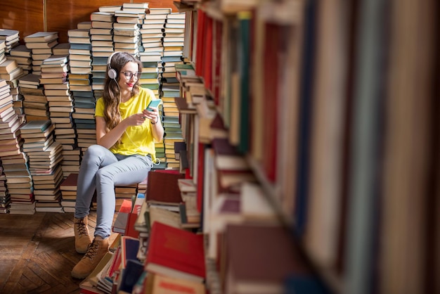 Estudiante joven sentada en el montón de libros en la antigua biblioteca