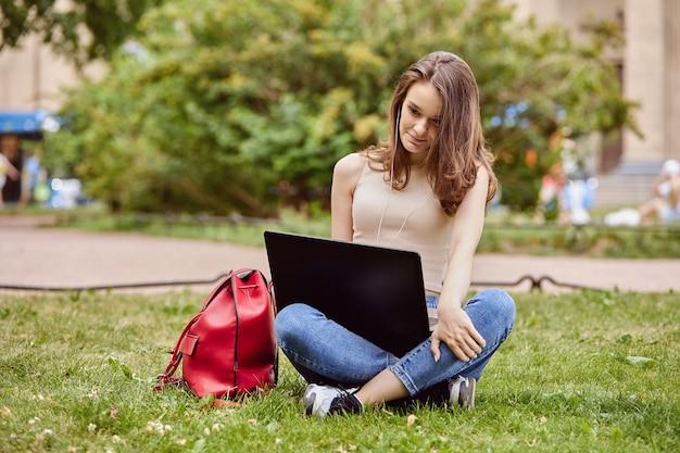 Estudiante con laptop se sienta en el parque en verano