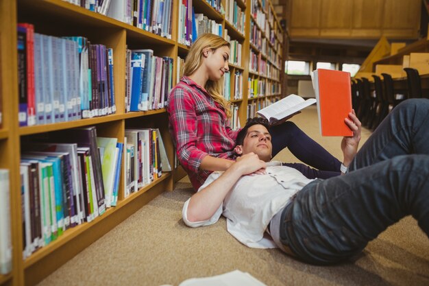 Estudiante leyendo un libro mientras yace en su compañero de clase en la biblioteca