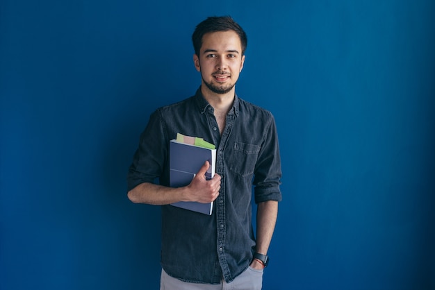 Estudiante con libro. Joven de pie y mirando a cámara.