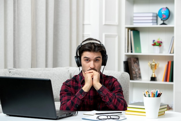 Estudiante en línea chico lindo en camisa a cuadros con gafas estudiando en la computadora mirando seriamente