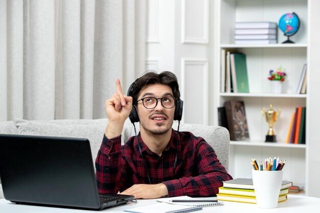 Estudiante en línea joven en camisa a cuadros con gafas estudiando en computadora en auriculares