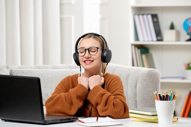 Estudiante en línea joven linda chica con gafas y suéter naranja estudiando en la computadora cerrando los ojos