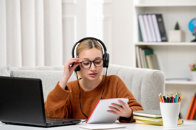 Estudiante en línea linda chica con gafas y suéter estudiando en la computadora con bloc de notas