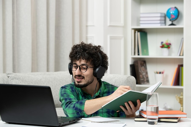 Estudiante en línea lindo joven estudiando en la computadora con gafas en camisa verde explicando notas