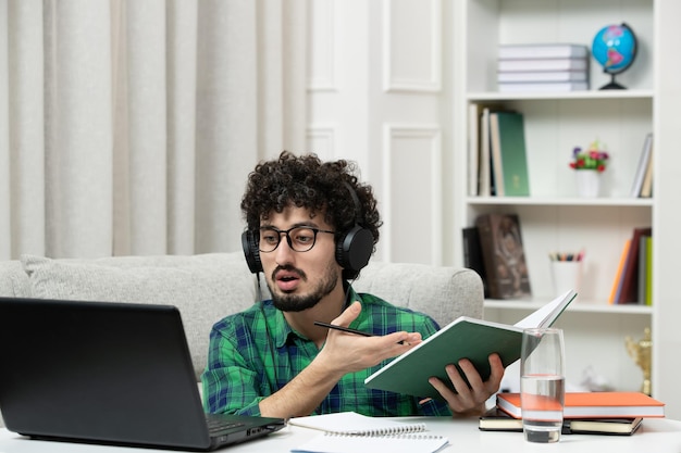 Estudiante en línea lindo joven estudiando en la computadora con gafas en camisa verde explicando notas