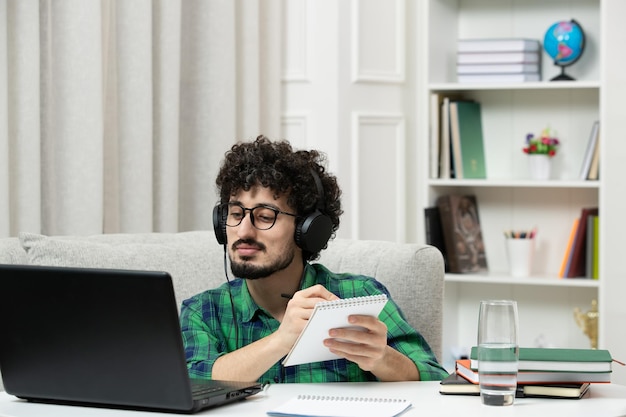 Estudiante en línea lindo joven estudiando en la computadora con gafas en camisa verde tomando notas