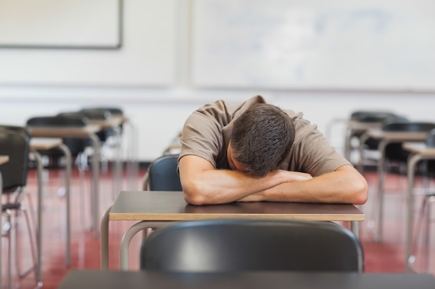 Estudiante maduro masculino que miente su cabeza en el escritorio mientras que duerme