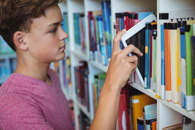 Estudiante manteniendo tableta digital en la estantería de la biblioteca