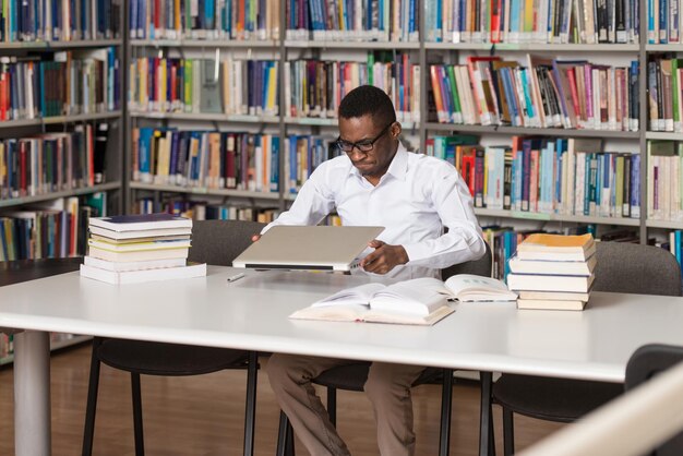 Estudiante masculino africano arrojando una computadora portátil y quiere destruirla con poca profundidad de campo