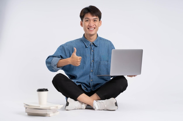 Estudiante masculino asiático de cuerpo completo usando una computadora portátil sobre fondo blanco