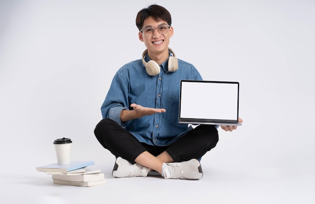 Estudiante masculino asiático de cuerpo completo usando una computadora portátil sobre fondo blanco