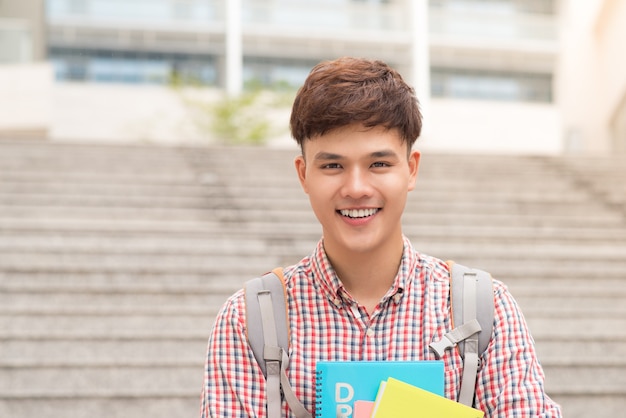 Estudiante masculino asiático de la universidad que sostiene el libro en el campus