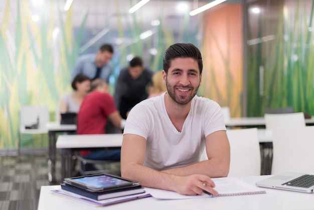 estudiante masculino en el aula trabajando en la tarea y aprendiendo con computadora portátil, grupo de estudiantes en segundo plano