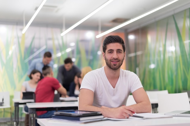 estudiante masculino en el aula trabajando en la tarea y aprendiendo con computadora portátil, grupo de estudiantes en segundo plano