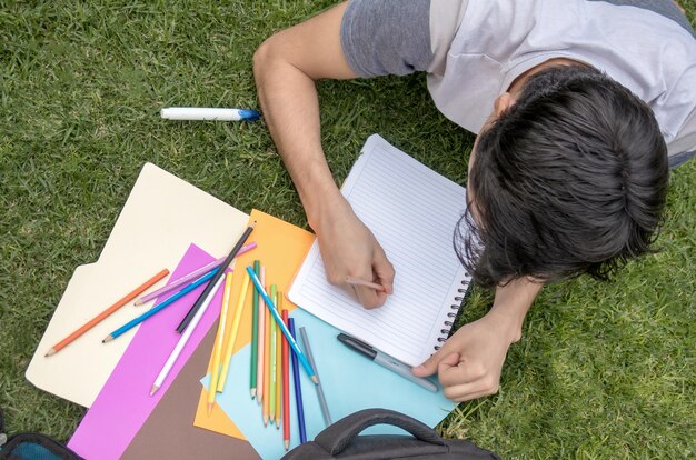 Un estudiante masculino escribiendo en un cuaderno en el césped