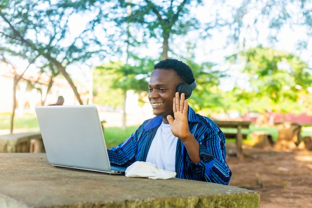 estudiante masculino feliz alrededor de la escuela usando una computadora portátil para el aprendizaje a distancia