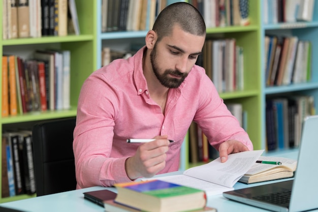 Foto estudiante masculino feliz trabajando con una computadora portátil en la biblioteca