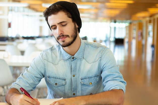 Foto estudiante masculino joven que estudia en la biblioteca.