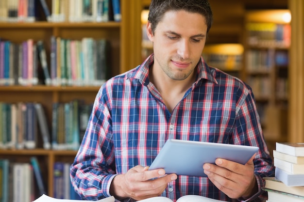 Estudiante masculino maduro concentrado que mira la tableta en la biblioteca