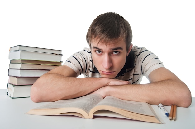 Estudiante masculino en la mesa con un montón de libros sobre blanco