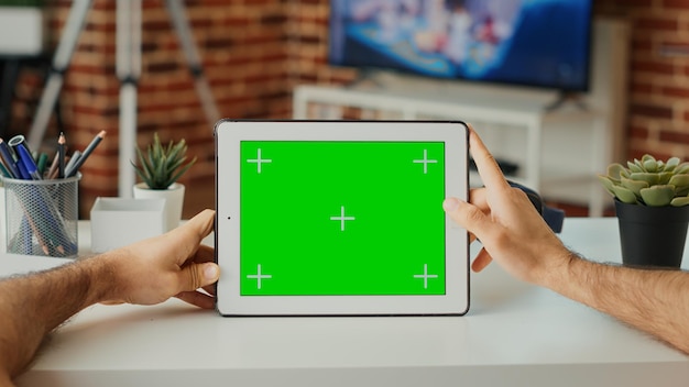 Estudiante masculino mirando la pantalla verde horizontal en pantalla, trabajando con un dispositivo digital en casa. Usando una plantilla de clave de croma aislada y un espacio de copia en blanco con una maqueta en la tableta. De cerca.