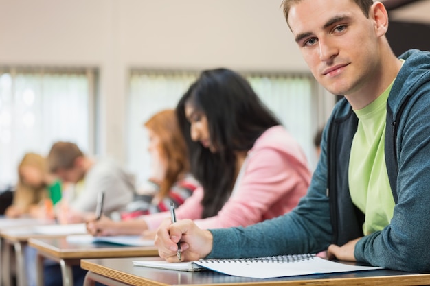 Estudiante masculino con otros escribiendo notas en el aula