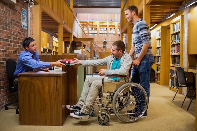 Estudiante masculino en silla de ruedas en el mostrador de la biblioteca