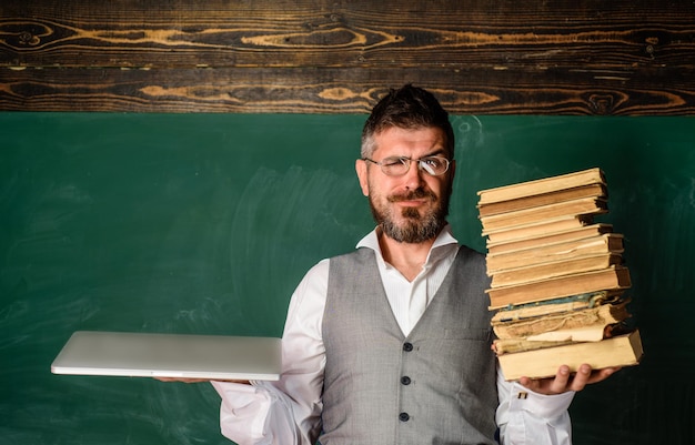 El estudiante masculino sonriente de la educación moderna sostiene el libro de texto tradicional y el libro electrónico de lectura vs el libro electrónico