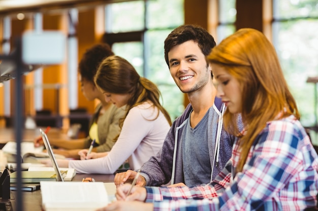 Estudiante mirando a la cámara mientras estudia con sus compañeros de clase