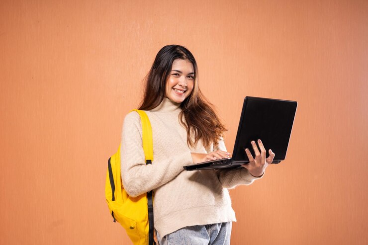 Foto un estudiante con una mochila usa una computadora portátil contra un fondo naranja vibrante