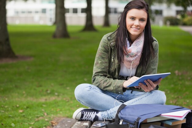 Estudiante morena feliz usando tableta sentado en el banco