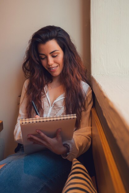 Estudiante mujer escribiendo en un cuaderno de un restaurante cerca de la ventana