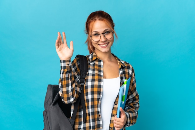 Estudiante mujer rusa aislada en azul saludando con la mano con expresión feliz