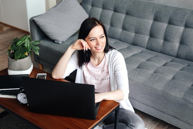 Foto estudiante mujer sentada en el piso de su apartamento con laptop y notas estudiando