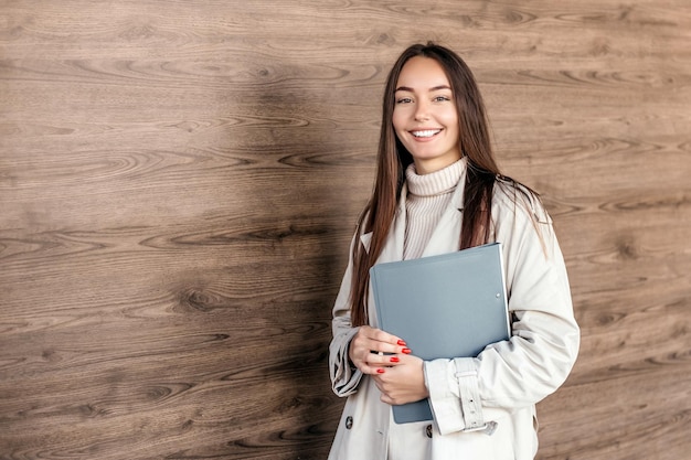 Estudiante mujer sonriendo y sosteniendo una carpeta contra el telón de fondo de la fachada del edificio