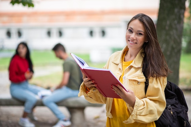 Estudiante mujer sosteniendo un libro frente a un grupo de amigos