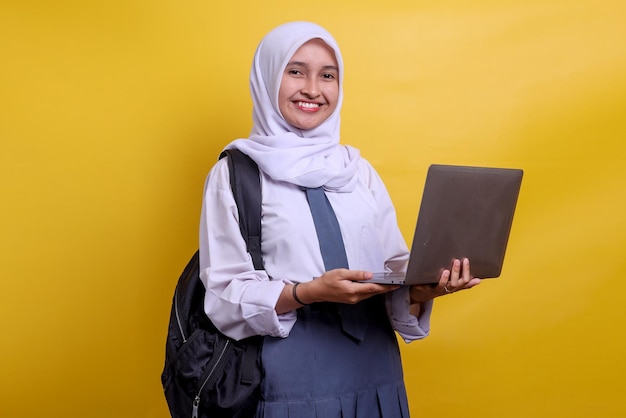 Estudiante musulmán de la escuela secundaria indonesia sonriendo y sosteniendo una computadora portátil
