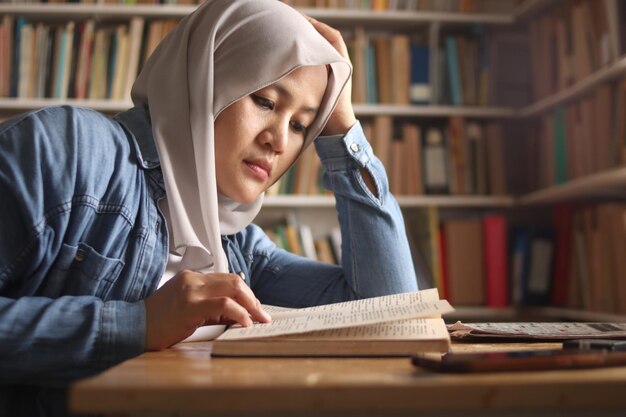 Estudiante musulmana asiática estudiando duro en la biblioteca leyendo libros para el examen cansada agotada