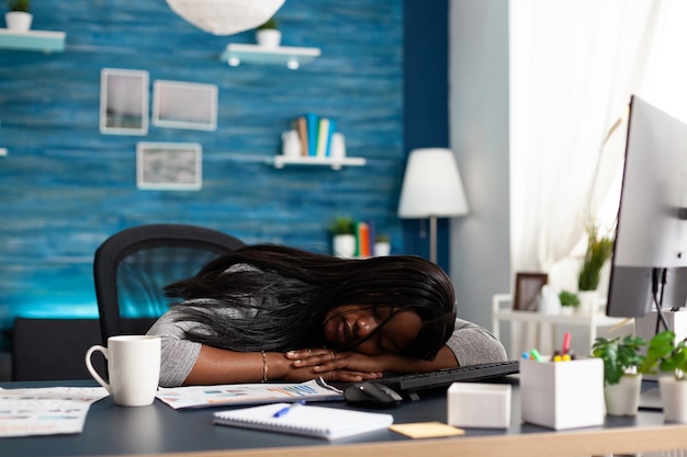 Estudiante negro adicto al trabajo cansado agotado durmiendo en la mesa de escritorio en la sala de estar