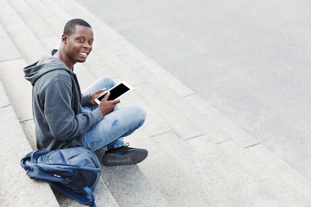 Estudiante negro feliz con tableta estudiando en las escaleras de la universidad