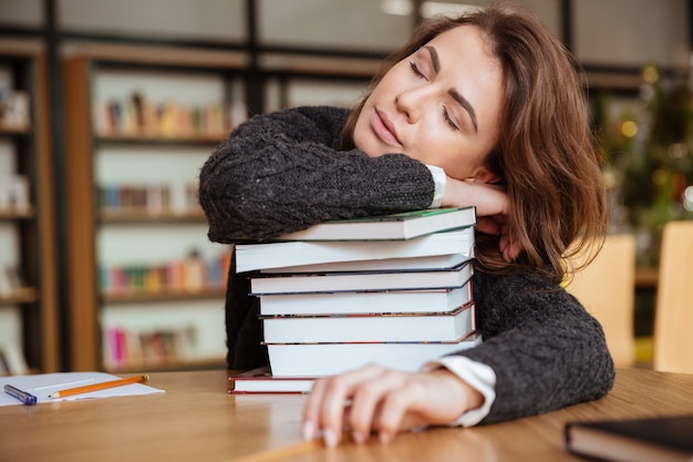 Estudiante niña o mujer joven con libros durmiendo en la biblioteca