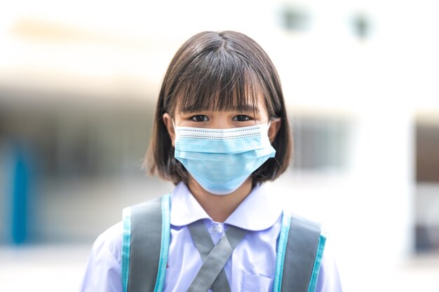 Estudiante de niños asiáticos alegre en uniforme de estudiante de regreso a la escuela con mascarilla médica después de la pandemia de COVID-19. Concepto De Regreso A La Escuela Stock Photo