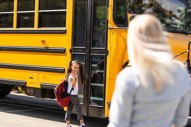 Estudiante de niños corriendo hacia las manos de su madre para abrazarla después de regresar a la escuela cerca del autobús escolar