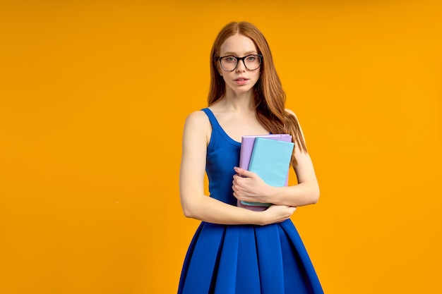 Estudiante o profesor diligente en anteojos de pie con libros en las manos, mujer educada e inteligente en anteojos mirando a la cámara con confianza, posando