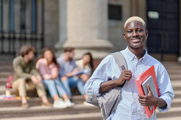Estudiante orgulloso con un libro de texto frente a la universidad