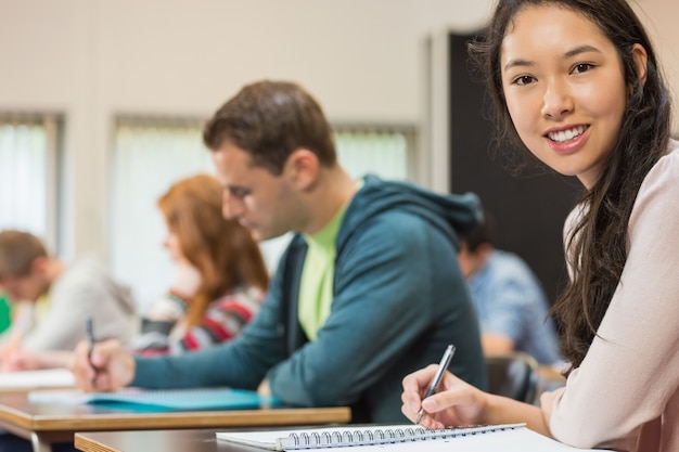 Estudiante con otros escribiendo notas en el aula