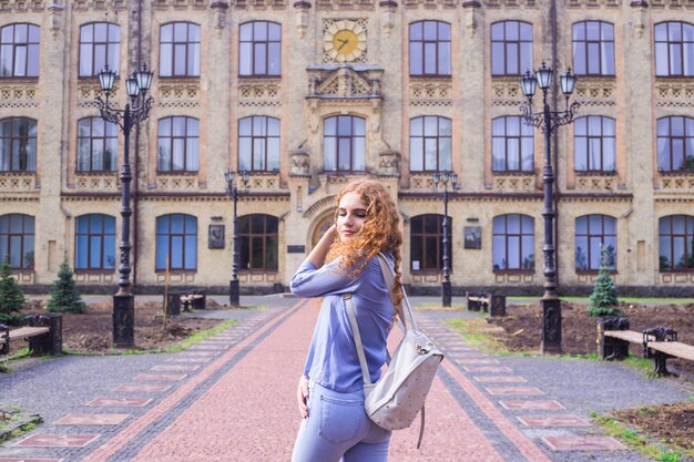 Una estudiante pelirroja de pelo rizado con una mochila en la espalda.