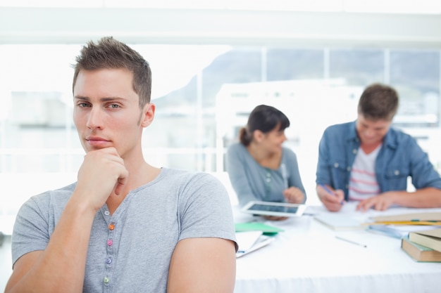 Un estudiante de pensamiento mirando a la cámara con sus amigos detrás de él